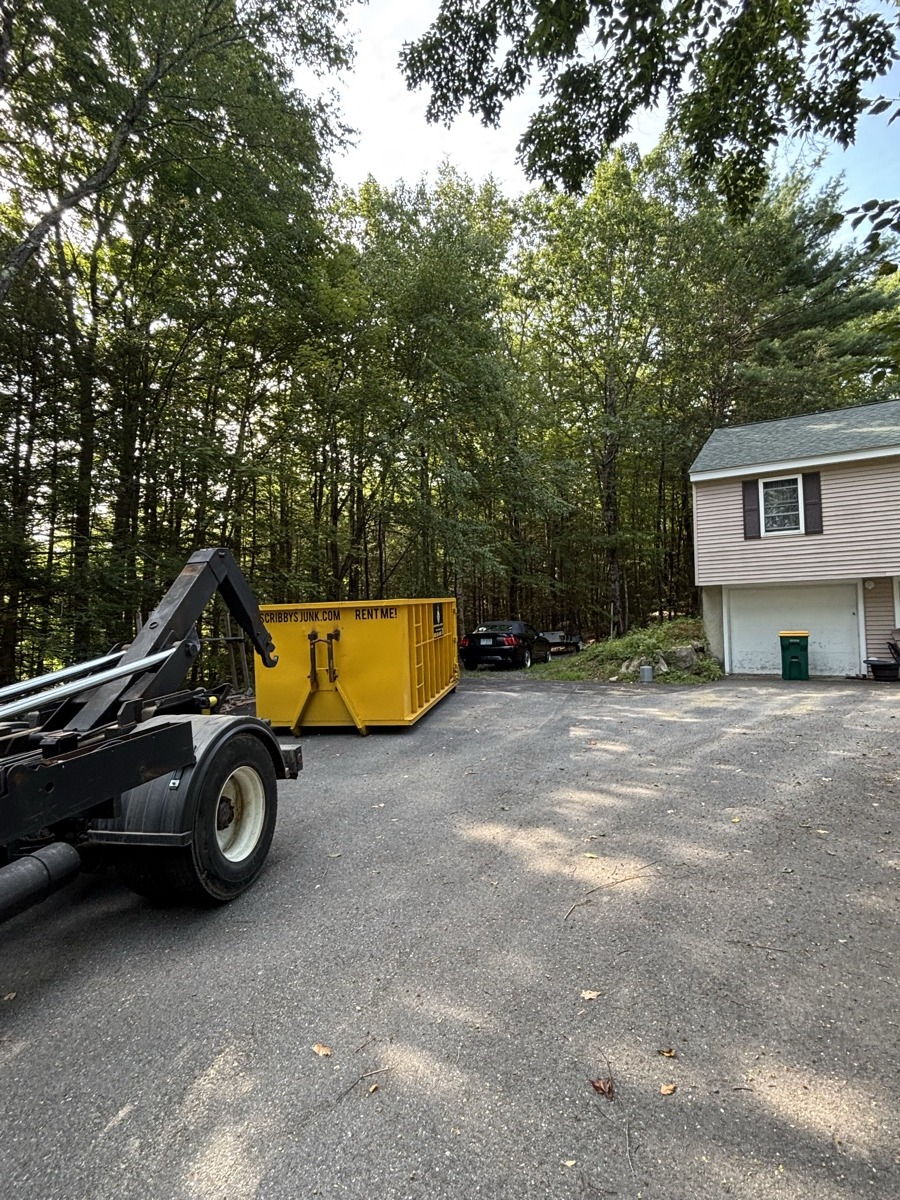 Yellow Scribby's 10-yard 'Rent Me' dumpster being placed by truck arm next to a small modular-style southern NH home.