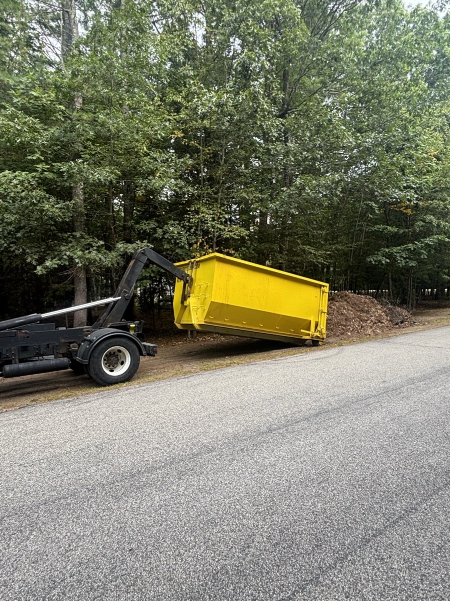 Empty yellow Scribby's 15-yard roll-off dumpster being placed on a clean asphalt driveway in southern NH, ready for loading.