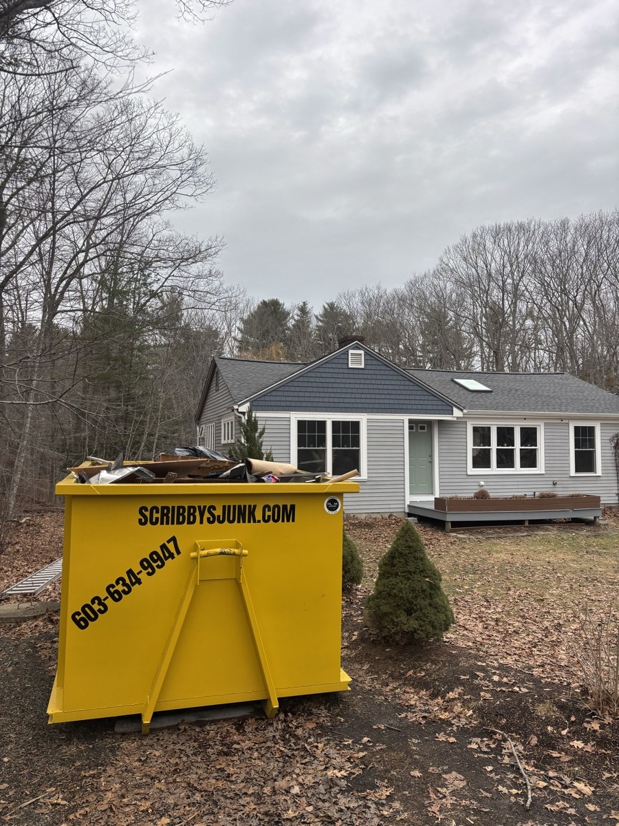 Yellow Scribby's 20-yard roll-off dumpster mid-fill with demolition debris in front of a gray colonial home in southern NH.