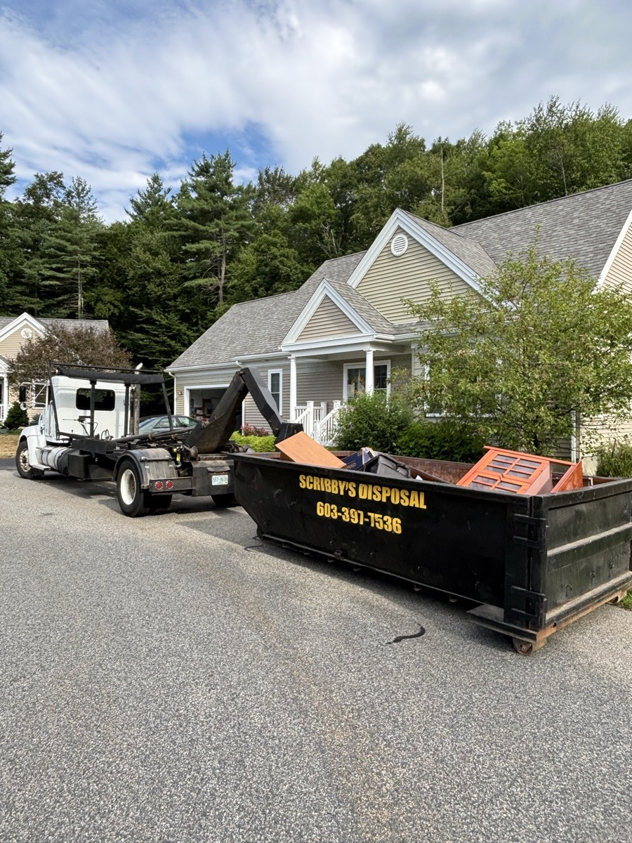 Scribby's 20-yard roll-off dumpster being placed by truck in front of a beige and stone-trimmed colonial home in southern New Hampshire.