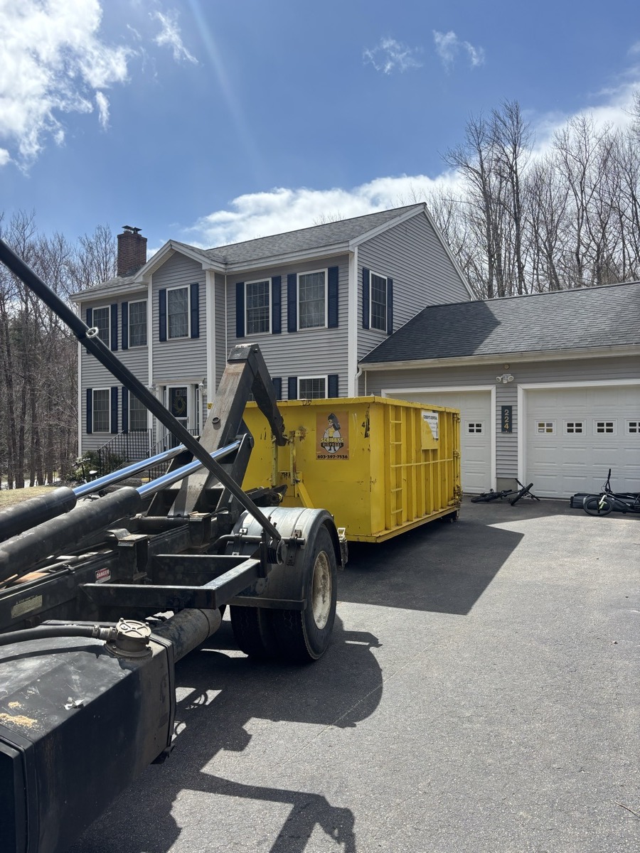 Yellow Scribby's 20-yard roll-off dumpster sitting empty on the driveway of a two-story white colonial home in southern New Hampshire.
