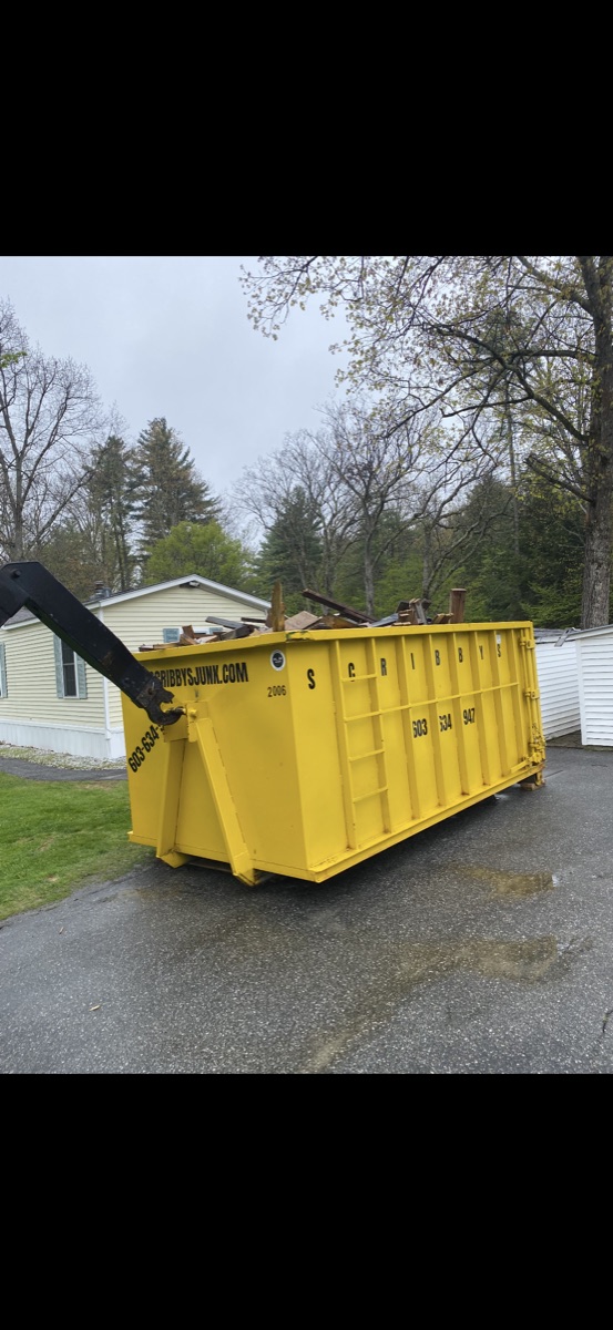 Brand-new yellow Scribby's 30-yard roll-off dumpster (unit 2006) on a paved driveway between two NH homes on a sunny spring day.