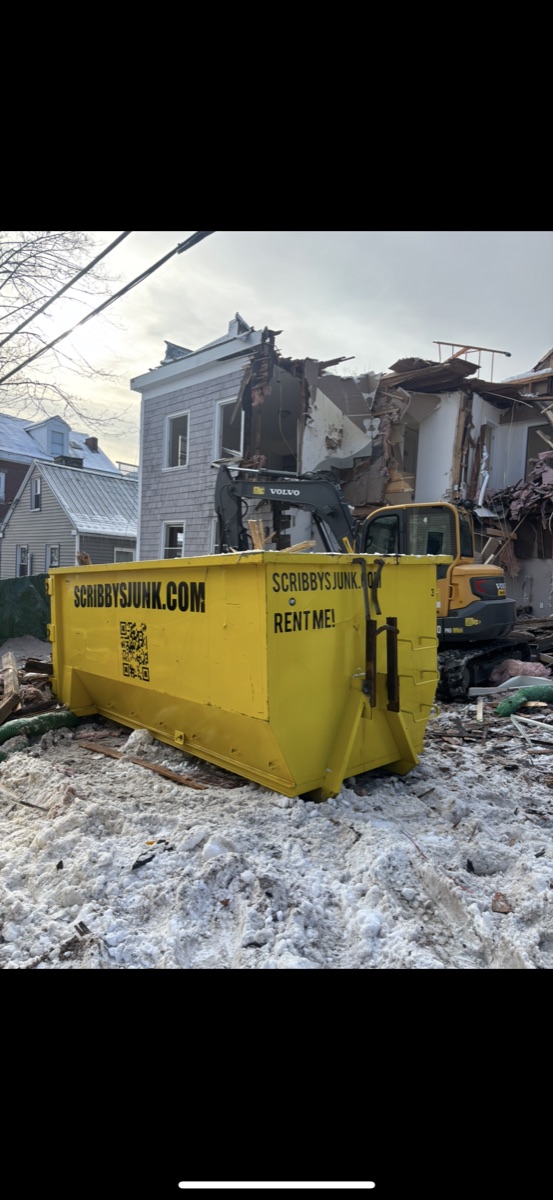 Yellow Scribby's roll-off dumpster and a Volvo mini-excavator at a partially demolished southern NH house at dusk — full tear-down cleanup.