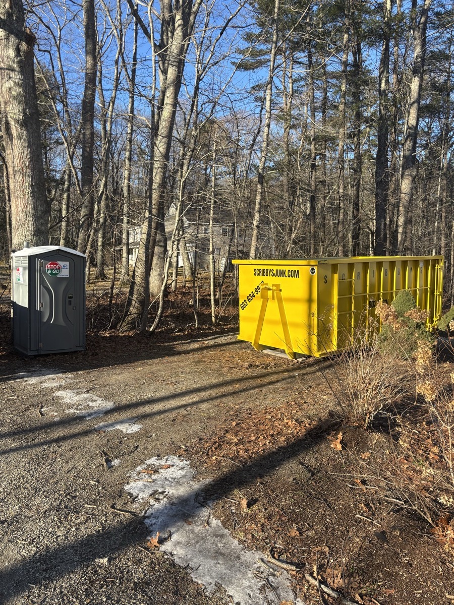 Empty yellow Scribby's roll-off dumpster on a truck parked on a dirt path in rural southern NH woods near a generator.