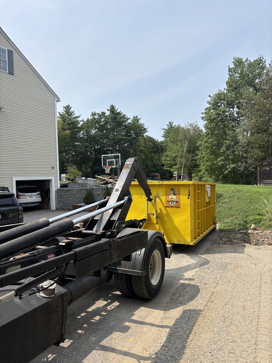 Yellow Scribby's Junk dumpster being delivered to a residential driveway with a basketball hoop in southern New Hampshire.