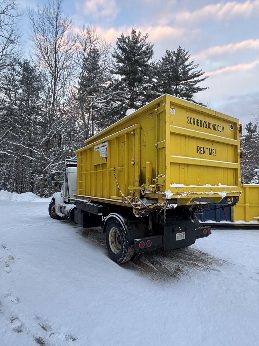 Yellow Scribby's roll-off dumpster mounted on a branded truck, parked on a snow-covered road at pink-and-blue sunset in southern New Hampshire.